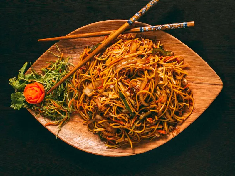 Fideos salteados con verduras en una bandeja de madera con palillos