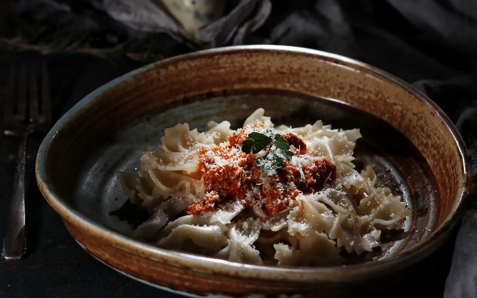 Plato de pasta con salsa y queso rallado en un cuenco de cerámica sobre una mesa oscura