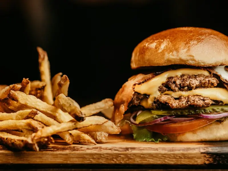 Hamburguesa con queso junto a patatas fritas sobre una tabla de madera